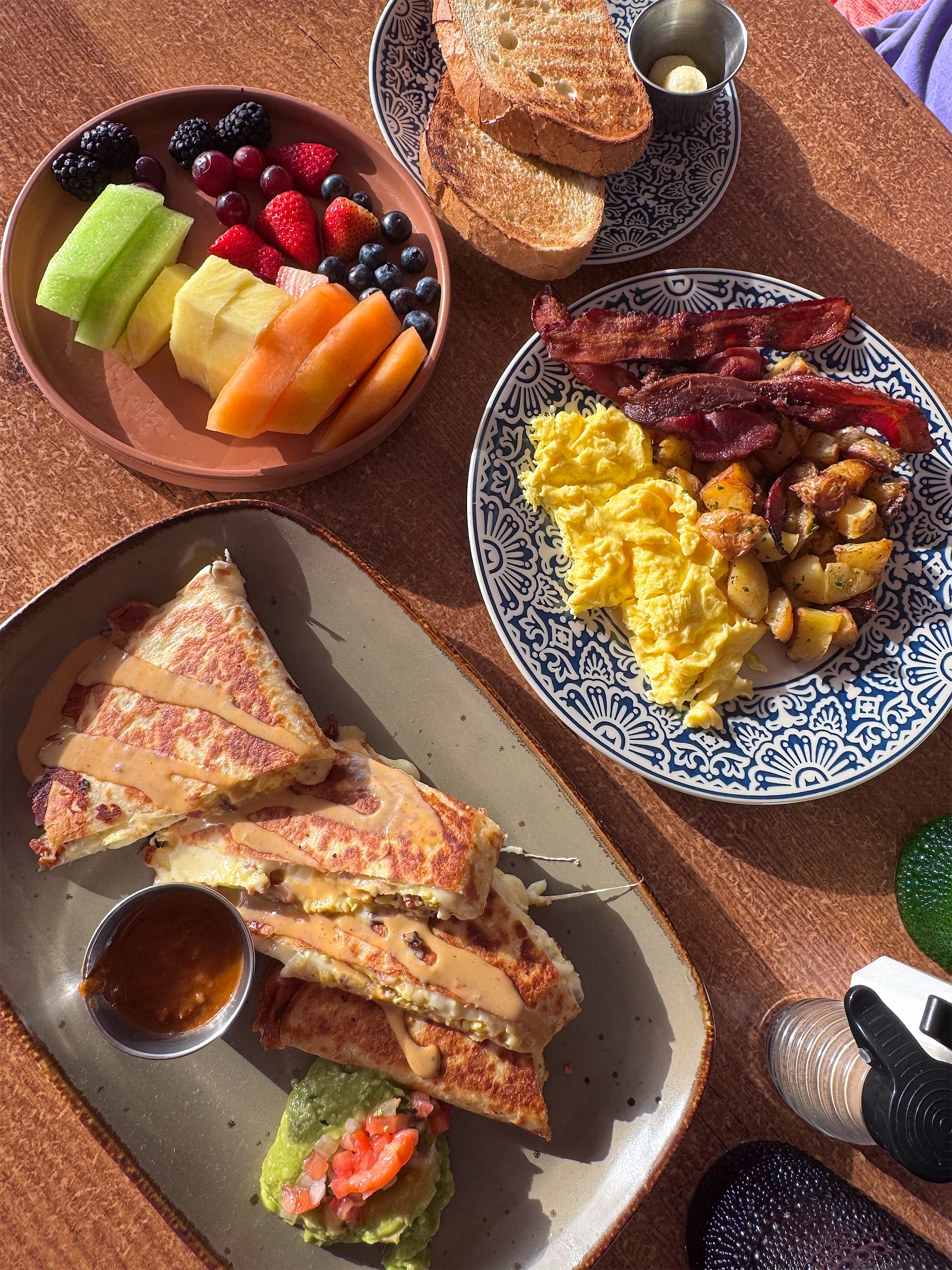 Overhead view of a big breakfast spread with fruit, eggs, bacon, and quesadillas