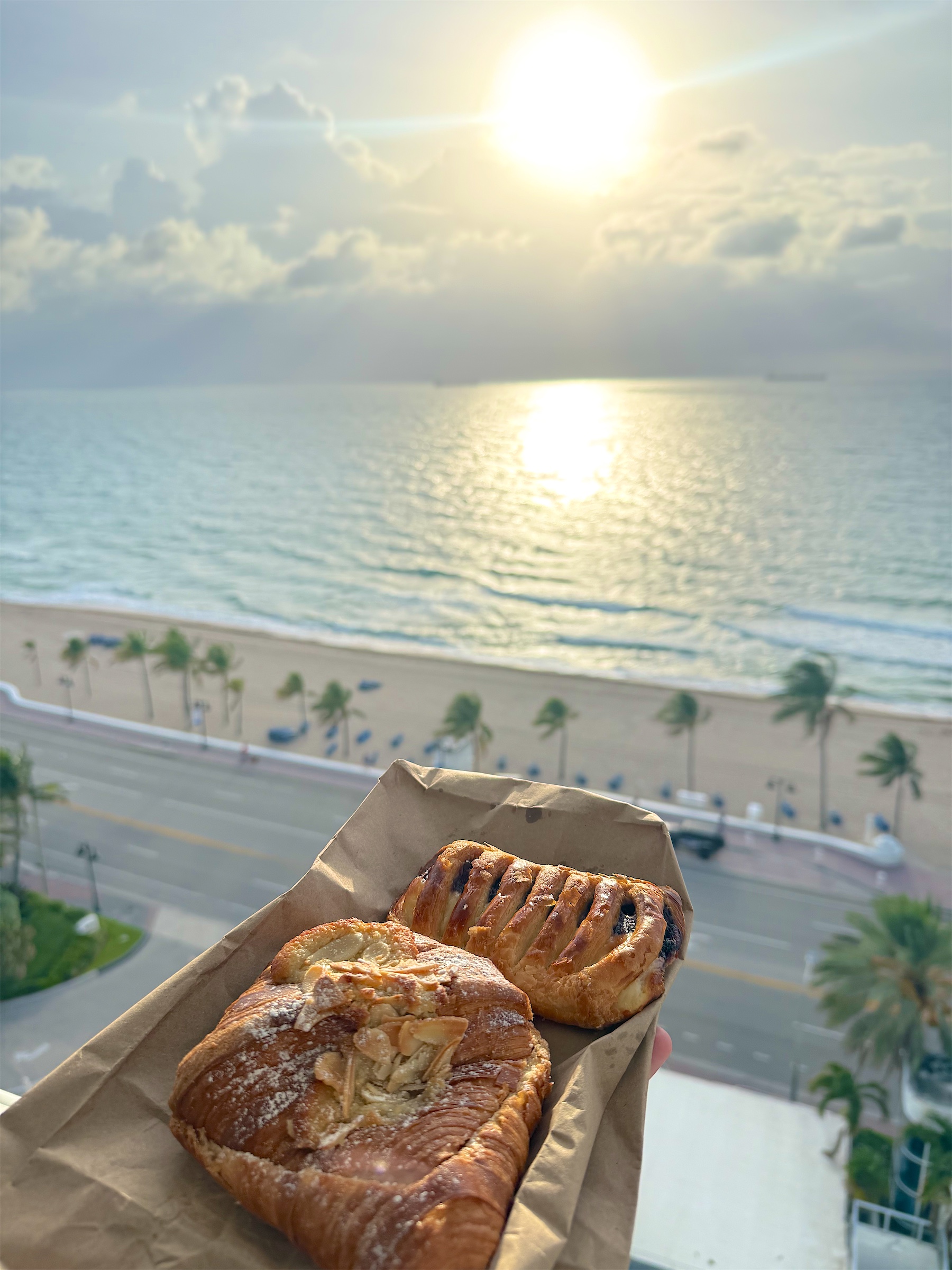 Fresh pastries held up over a beach and sunlit ocean