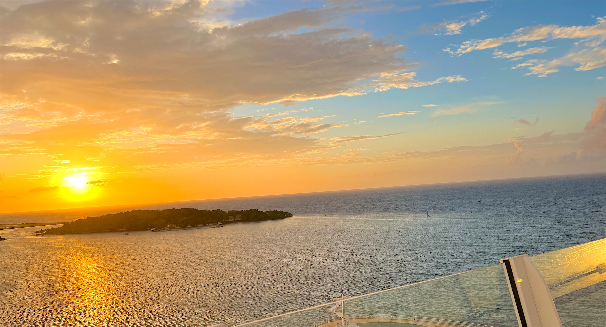 A golden sunset over the sea and a small island, seen from the top of a cruise ship