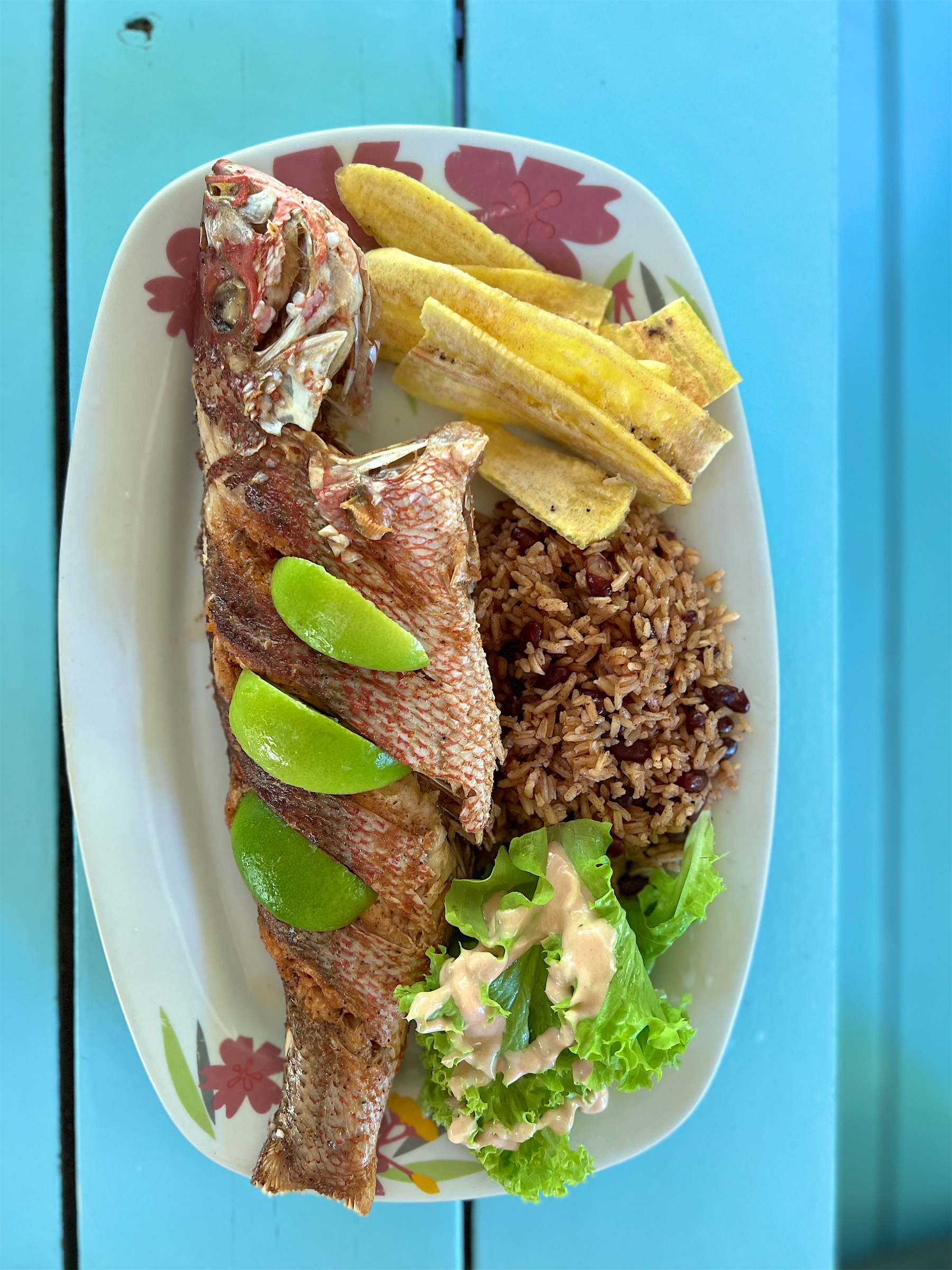 A whole fried fish with plantains and rice on a turquoise table