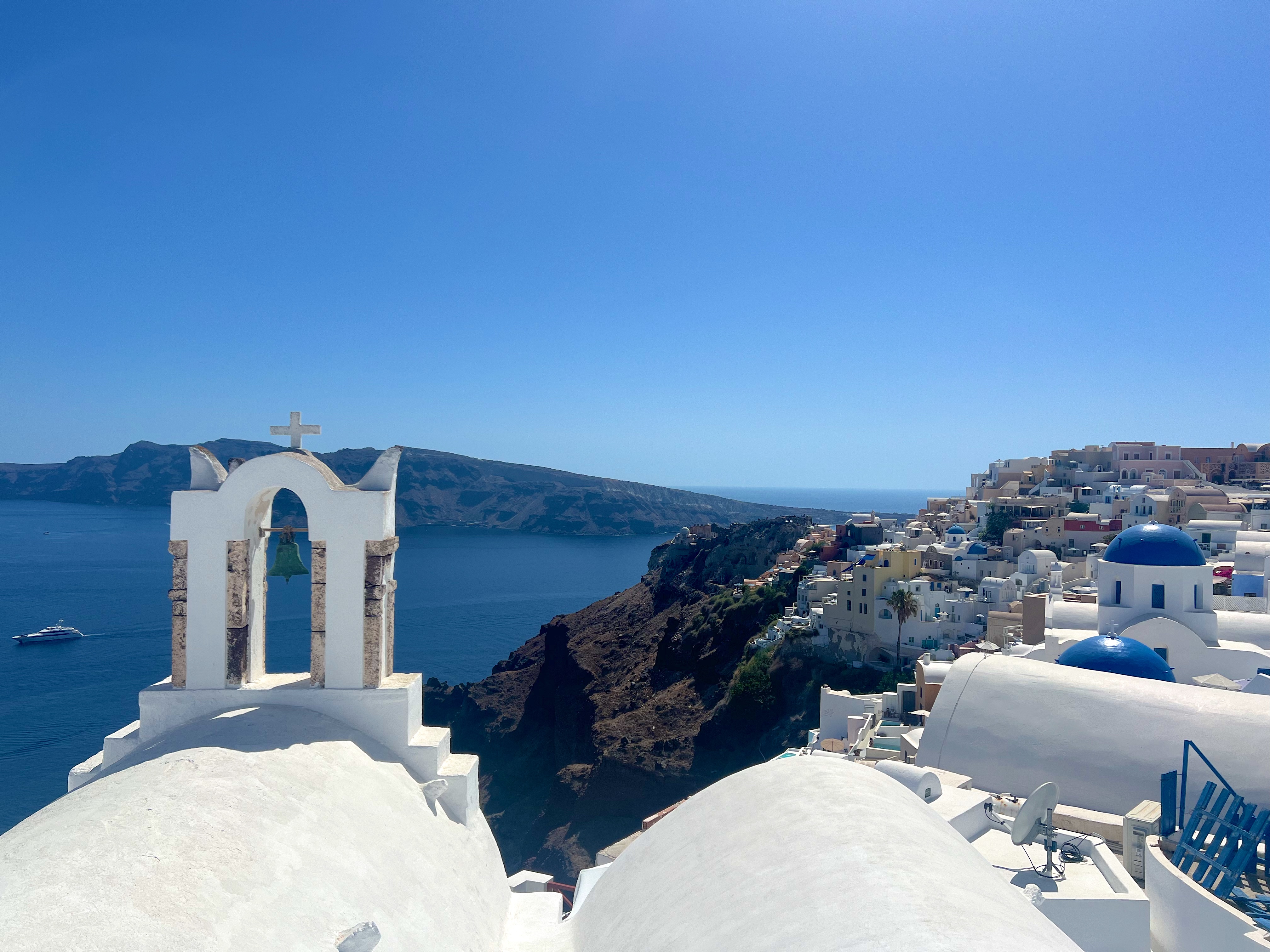 A white bell tower and blue domes above the sea in Oia, Santorini