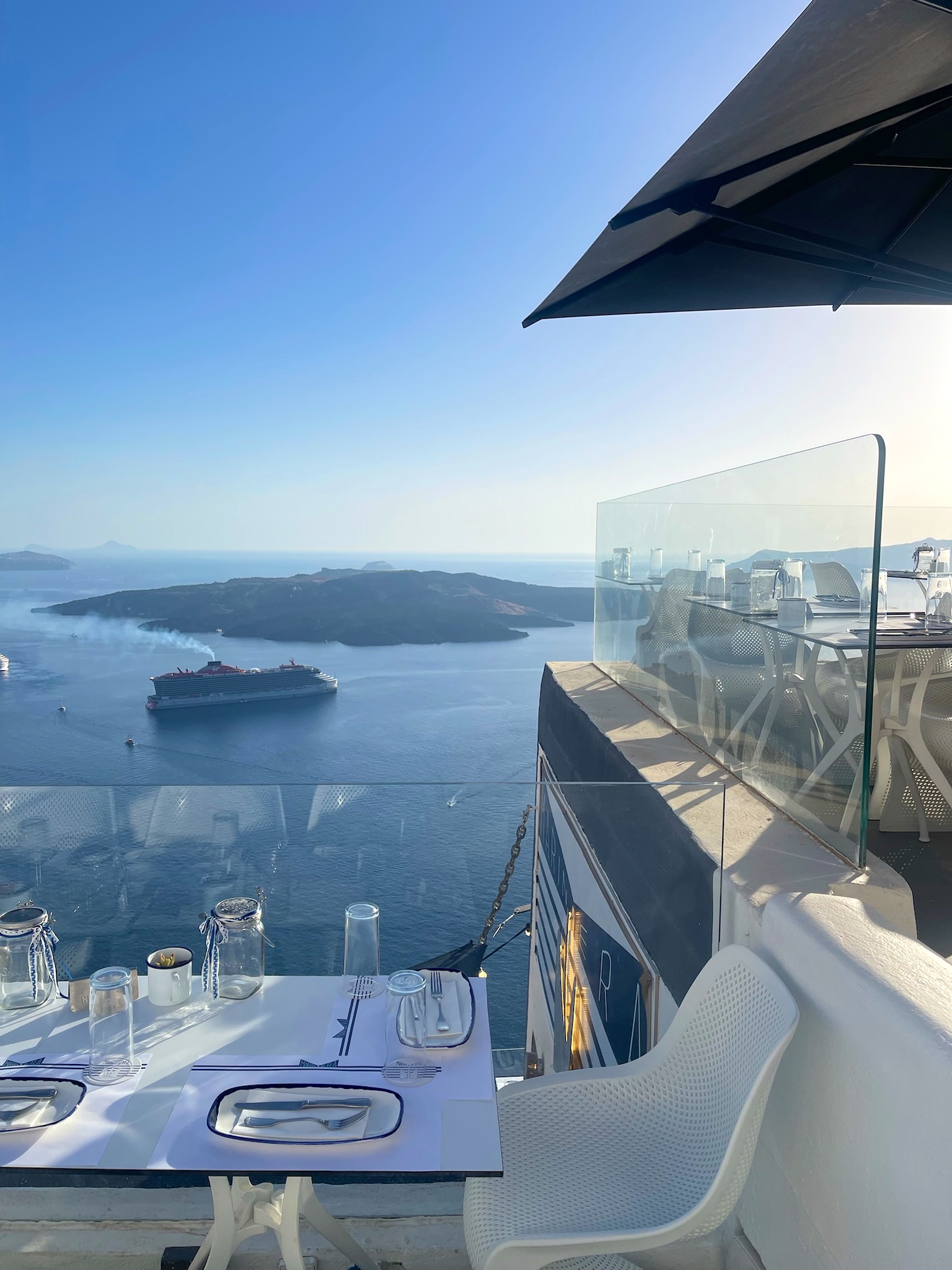 A table set for dinner above the Santorini caldera with a cruise ship in the water below