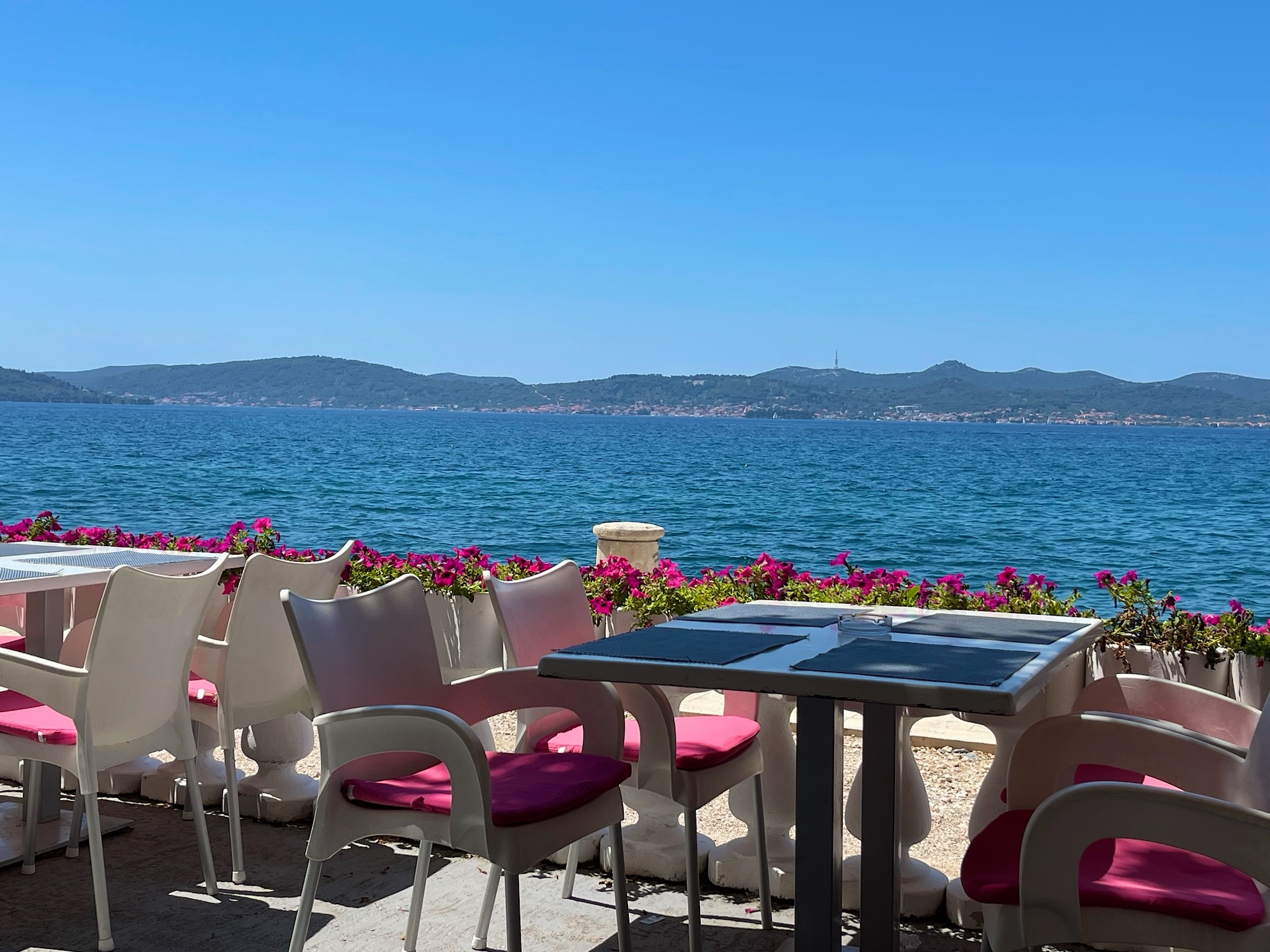 A seaside terrace with pink flowers overlooking bright blue water