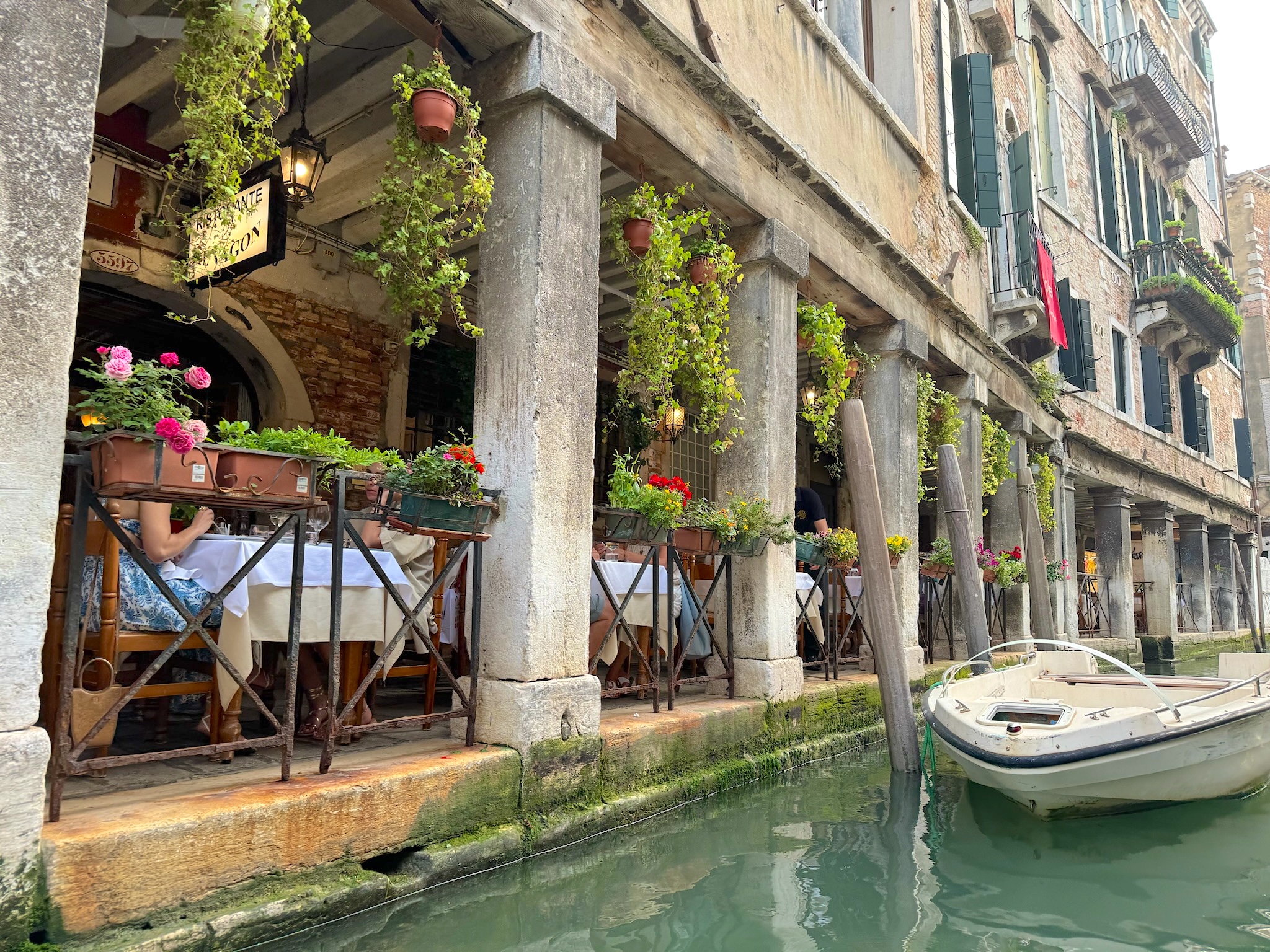 Canalside restaurant tables among flowers and stone columns in Venice